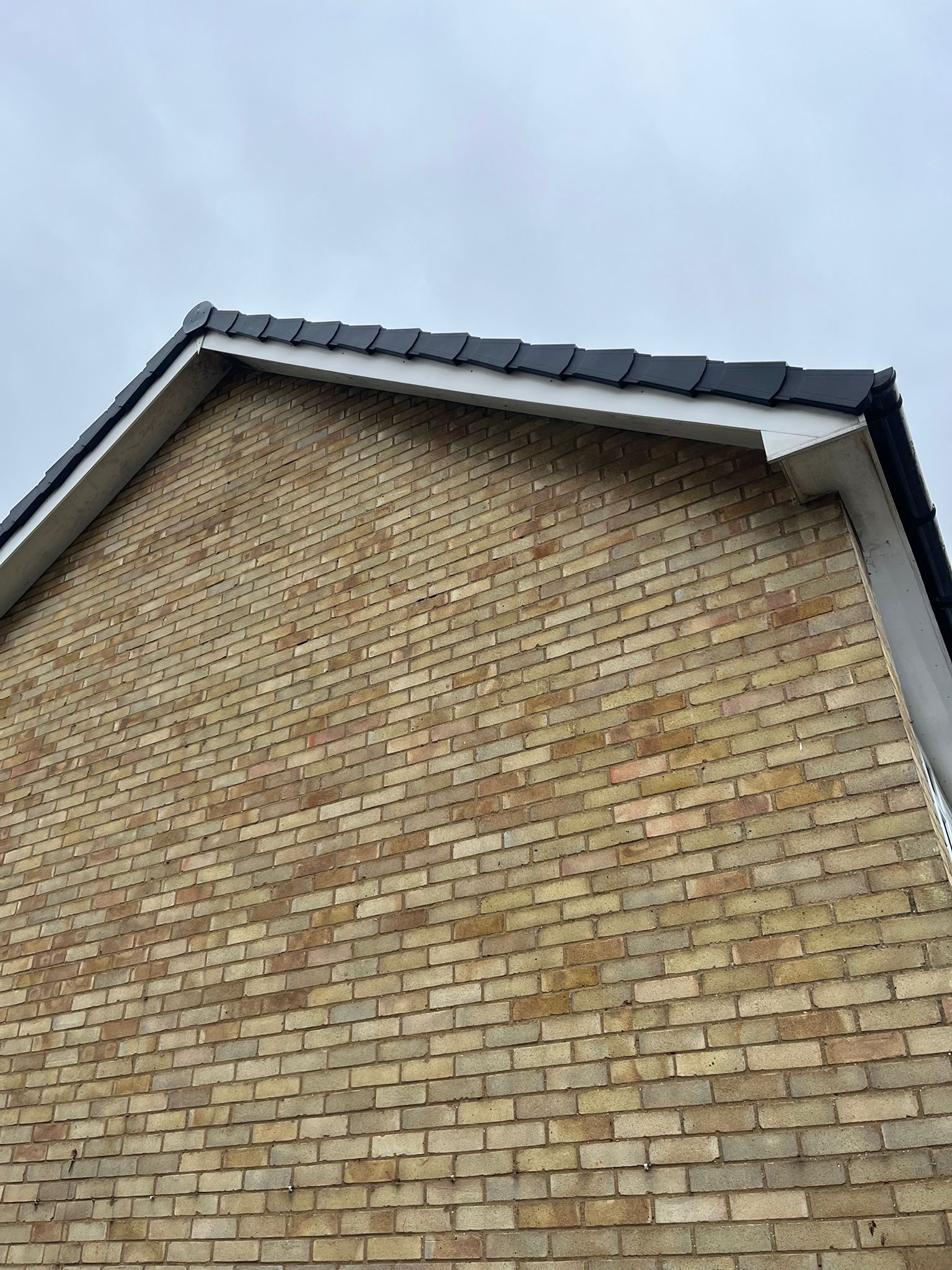A finished roof verge by Belstead Roofing showing new grey ridge tiles and clean white fascia against a brick gable